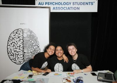 Three students smiling at the camera in front of AU Psychology Student sign