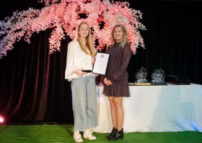 Two students on stage holding Best in Business certificate and trophy