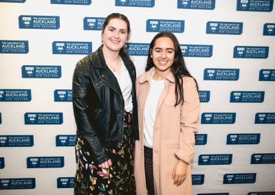 Two young women in front of wall with University of Auckland logos